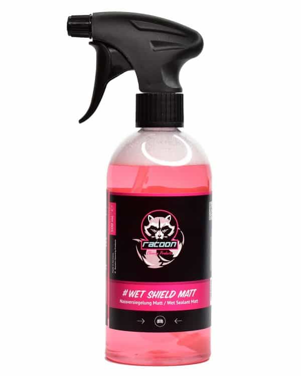 průhledná láhev s rozprašovačem obsahující růžově čirou tekutinu, přípravek určený jako tekutý vosk při mytí automobilů s matným lakem nebo fólií Wet Shield Matt, s etiketou a logem autokosmetiky Racoon Cleaning Products